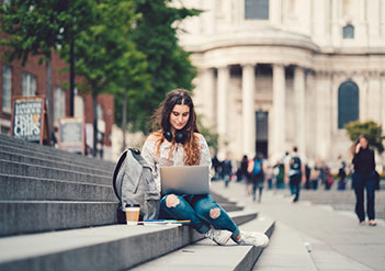 Woman sitting on the stairs of a building working on her laptop